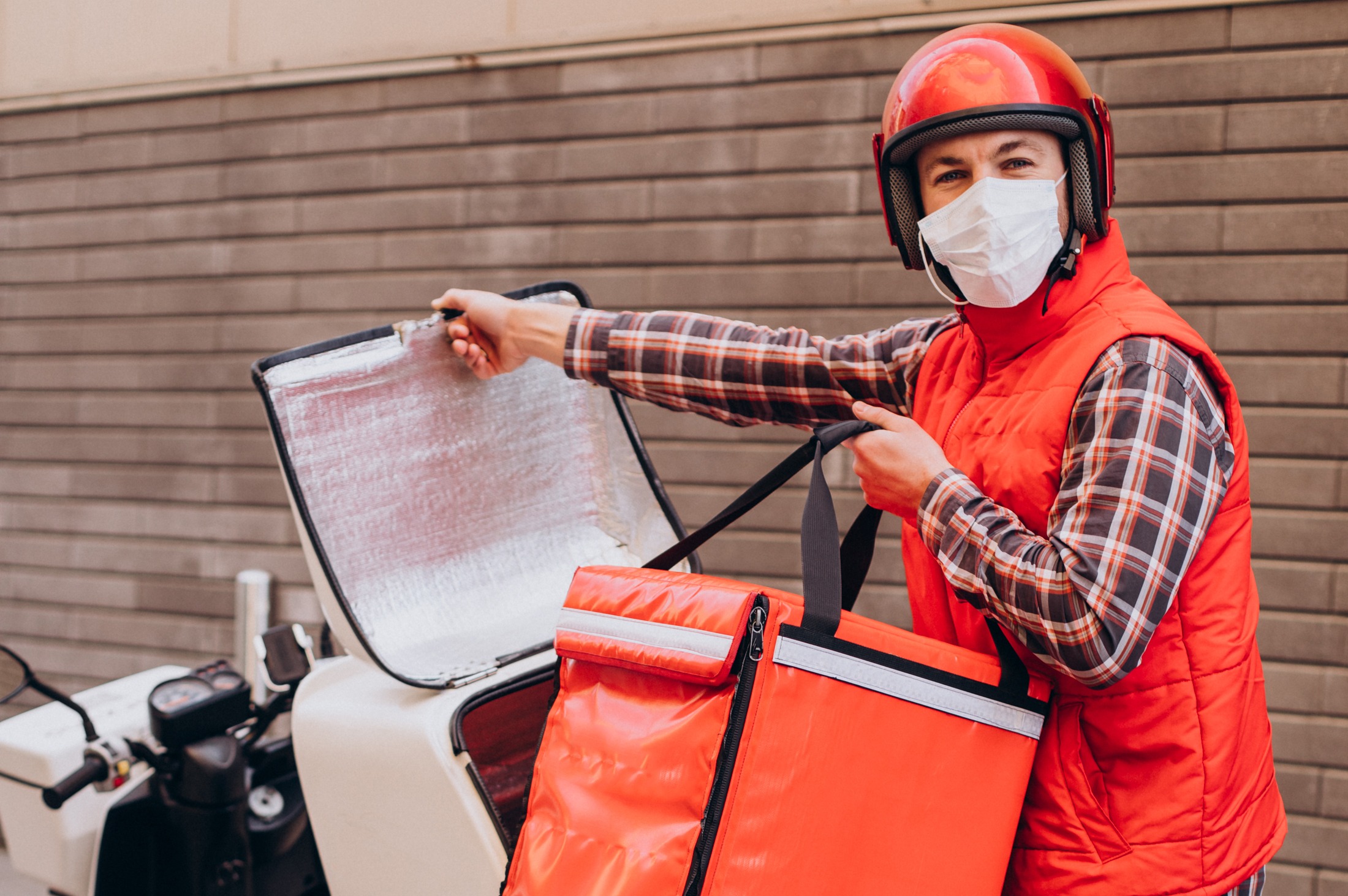 Food delivery boy driving scooter with box with food and wearing mask